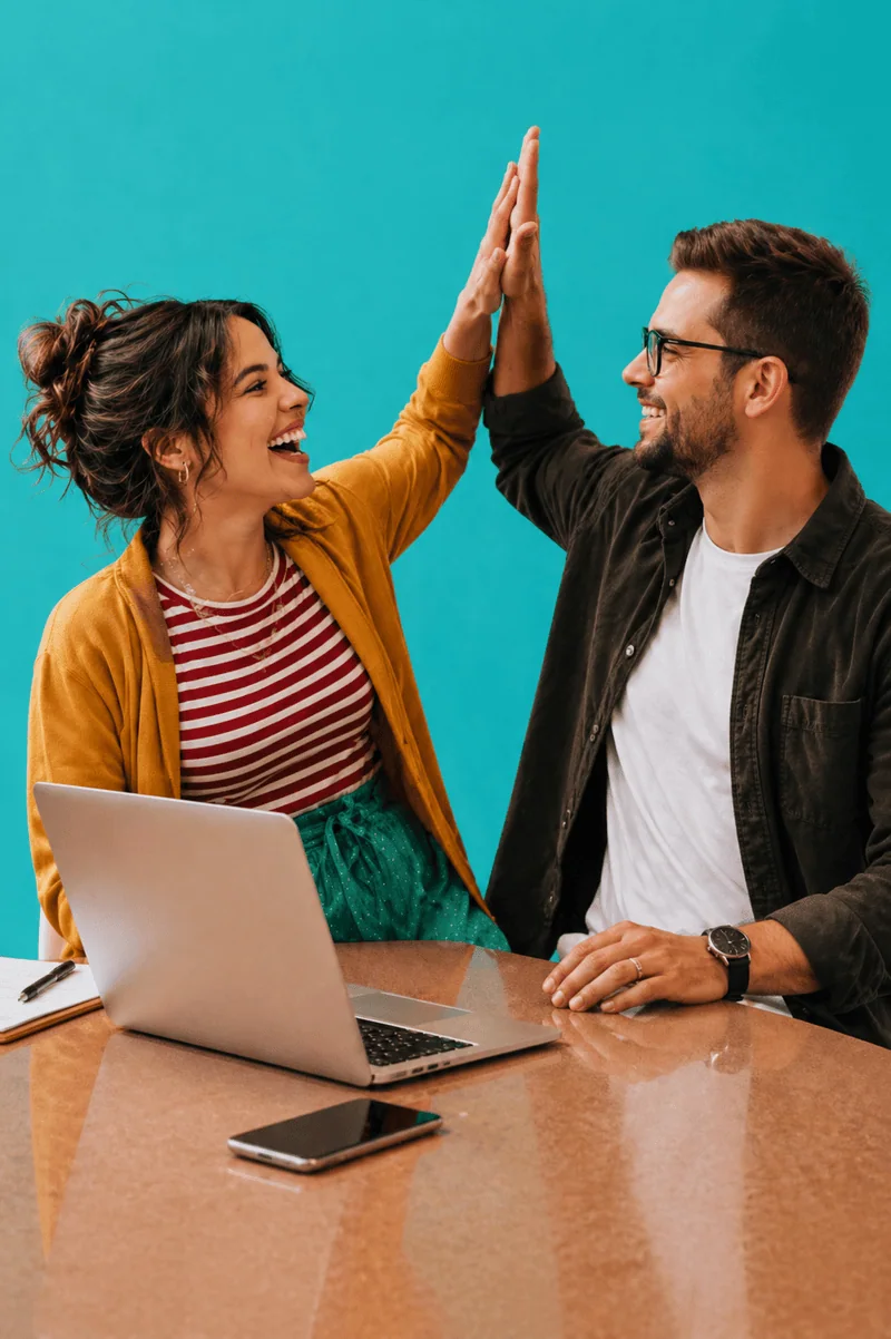 Two people collaborating on a laptop and high-fiving, representing custom website design and successful project completion